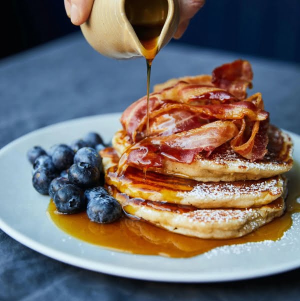 Pancakes on plate, blue berries, bacon, maple syrup pour