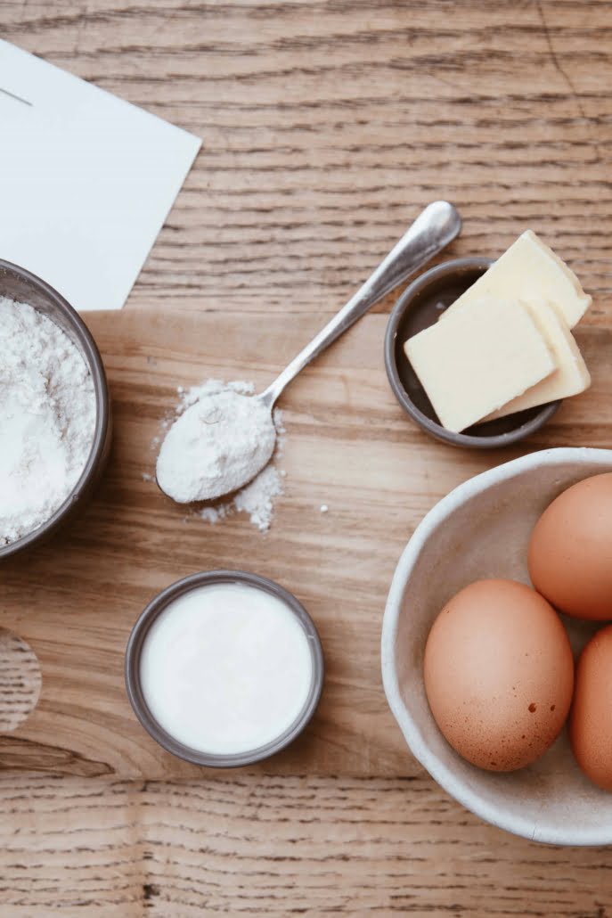 Ingredients to pancake mix laid out on wooden table, includes butter, eggs, flour, buttermilk